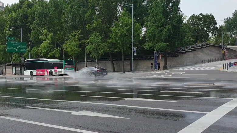 Road studs spraying water while a black car and a bus passes by
