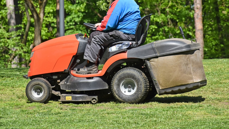 A man using a riding mower to cut grass with front and rear wheels visible