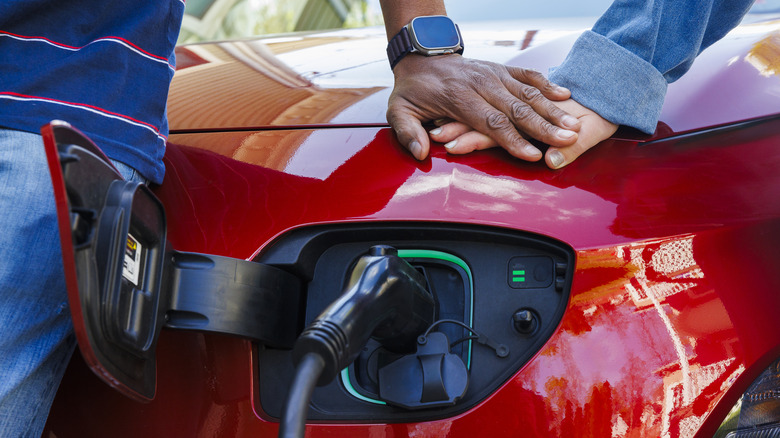 Multi-racial family's hands resting on a red electric vehicle that is being charged.