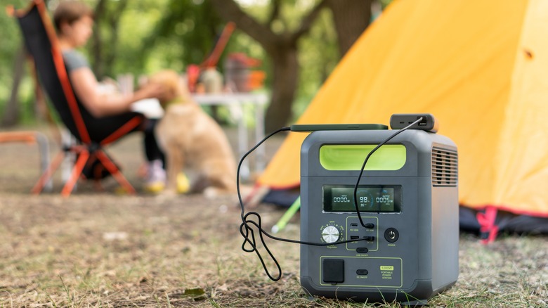 Portable power station with lithium ferrophosphate battery charging electronic devices used at a wild camp site, in front of yellow tent.