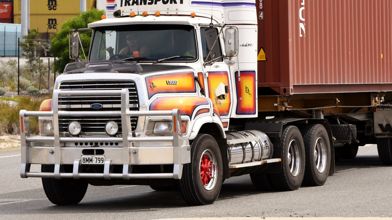A white Ford L9000 with colorful graphics and a trailer on the move, front 3/4 view