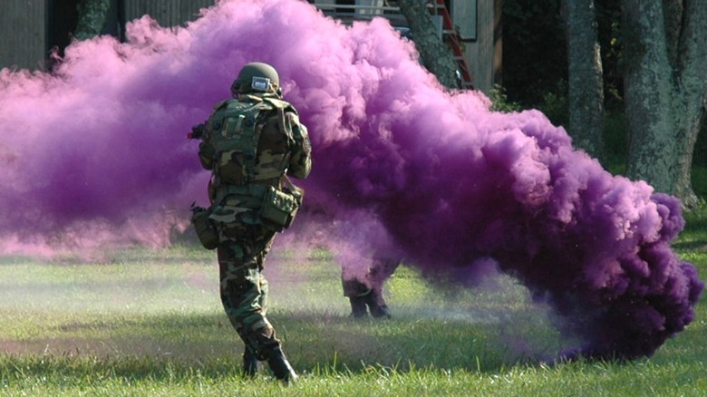 Airmen moving past a purple gas grenade's cloud