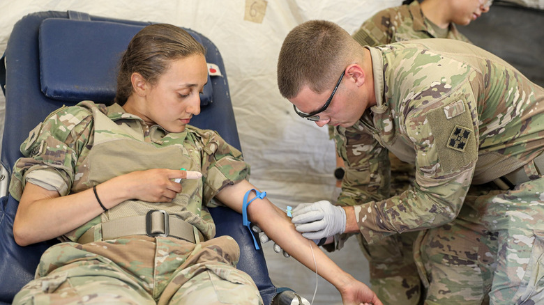 Combat medic takes blood from arm of serviceperson.