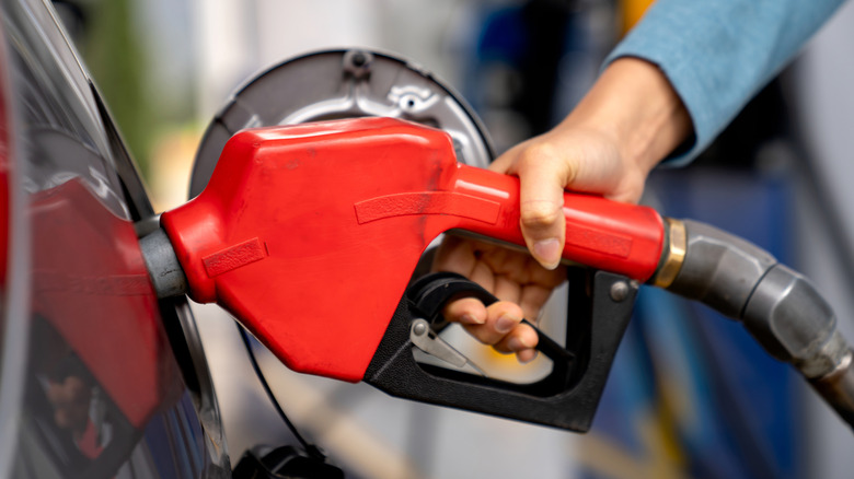 Person holding on to a red gas pump nozzle while filling up a car