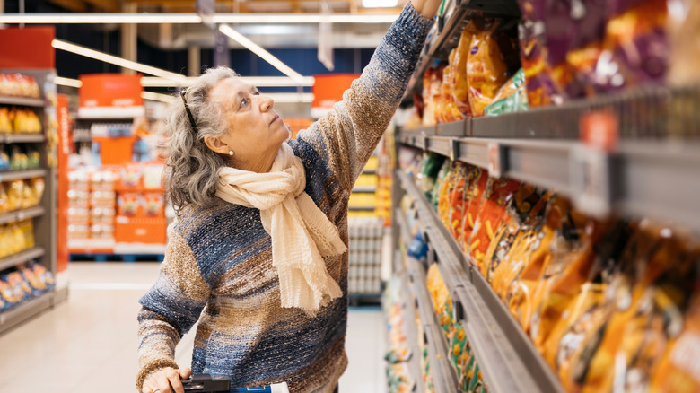 Woman in a convenience store reaching up for groceries on a shelf