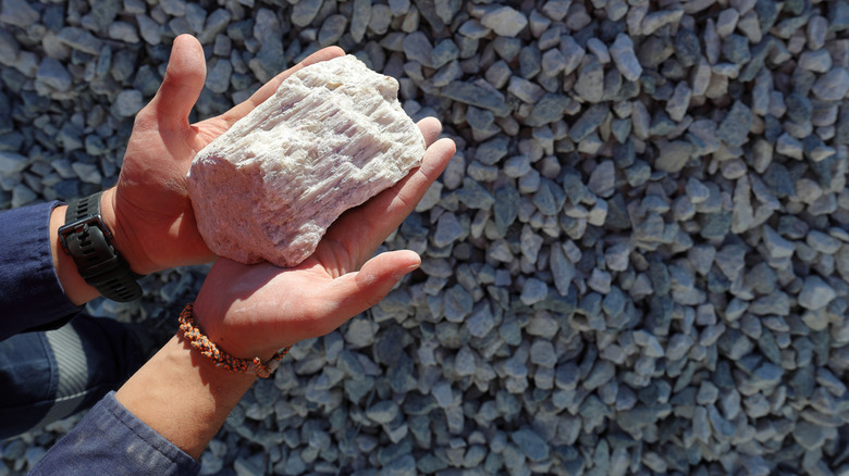 Hands holding spodumene ore, a lithium bearing mineral, above small rocks.
