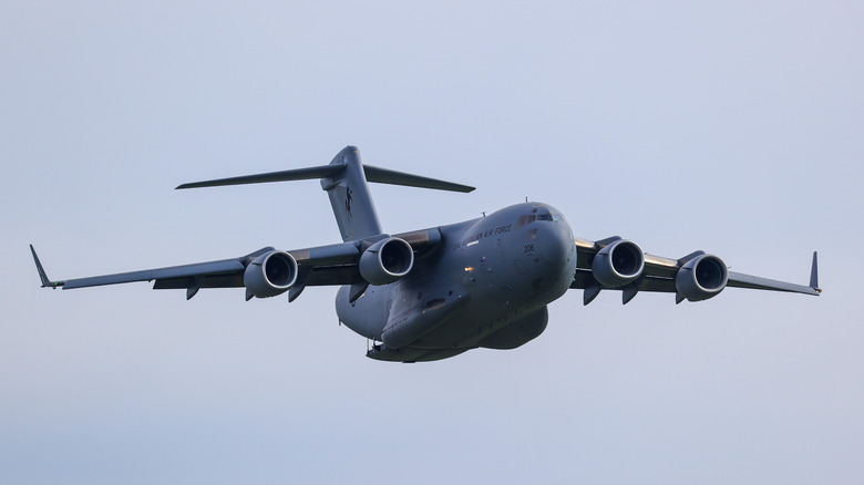 A Boeing C-17 Globemaster III flies across a cloudy sky