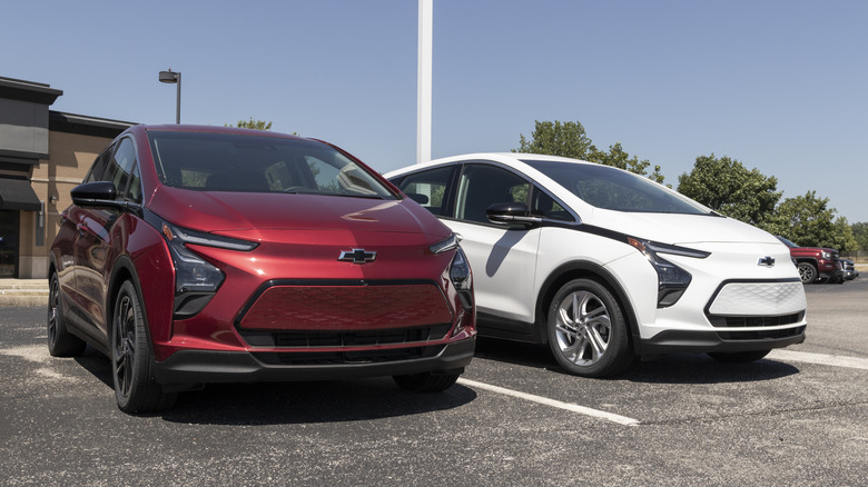 Front 3/4 view of red and white Chevy Bolt EVs parked on dealer lot.
