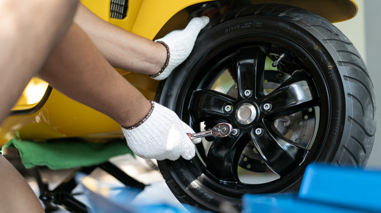 A person using a socket wrench to unbolt the wheels on a Vespa