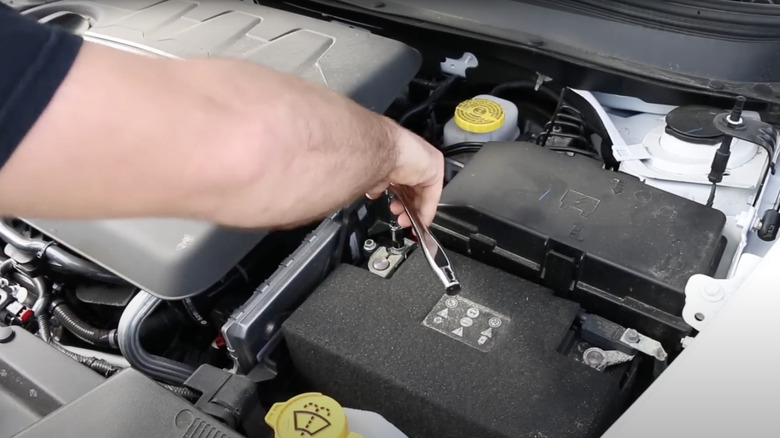 A person using a Milwaukee Four Flat socket wrench under the hood of a car