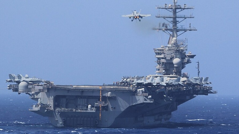 The USS Nimitz on the open ocean with a fighter jet coming in to land.