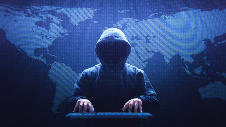 Hooded figure representing a hacker with hands on keyboard