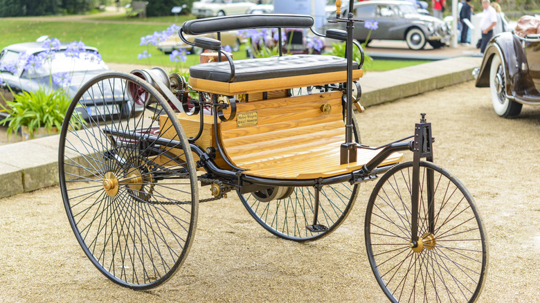 A Benz Patent-Motorwagen parked outside.
