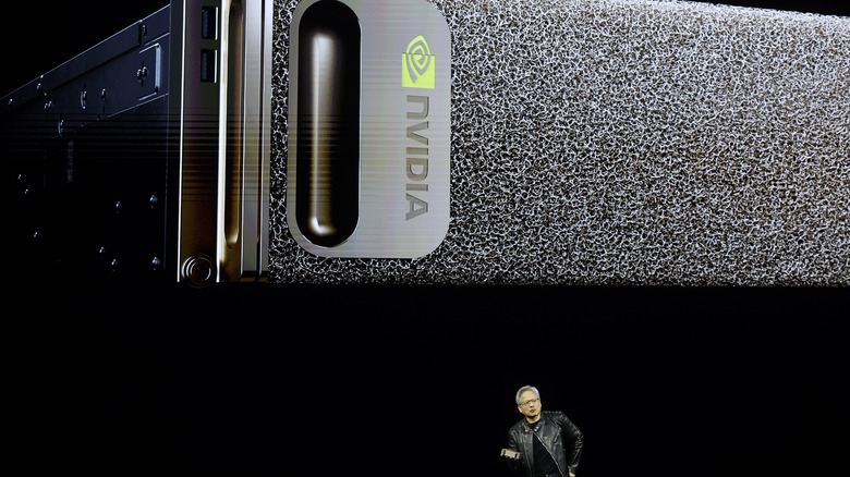 Nvidia CEO Jensen Huang onstage holding a DGX with a large picture of a DGX as a backdrop