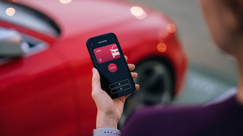 Car app open on a smartphone next to a vehicle