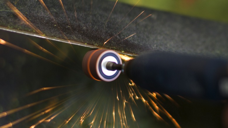 Using a rotary tool to sharpen a lawn mower blade.