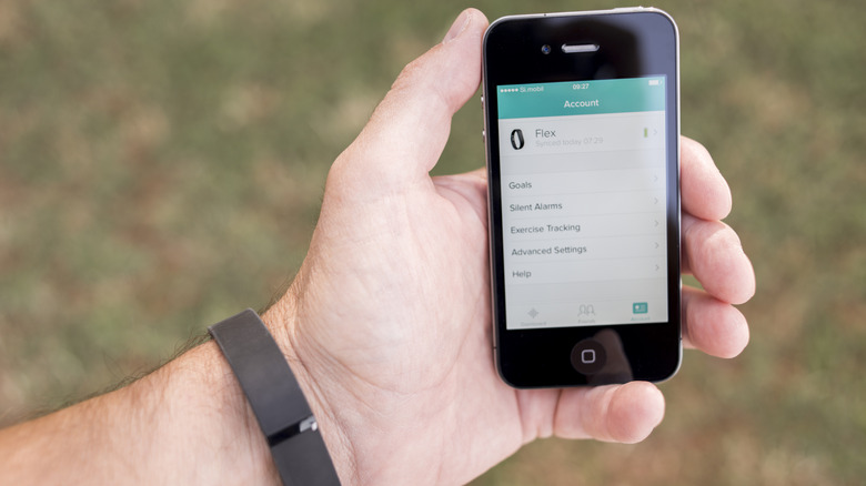 Rastreador de fitness Fitbit em um braço e aplicativo Fitbit no iPhone