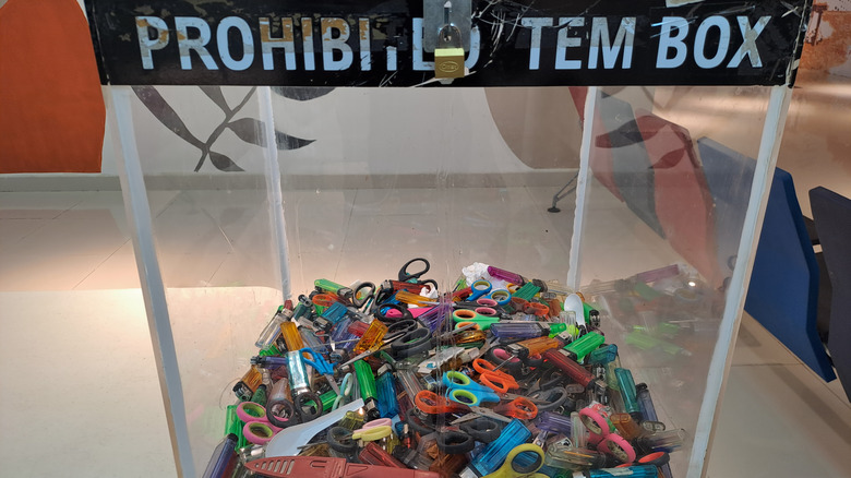 Glass disposal box of prohibited items at an airport, mainly containing scissors and disposable lighters.