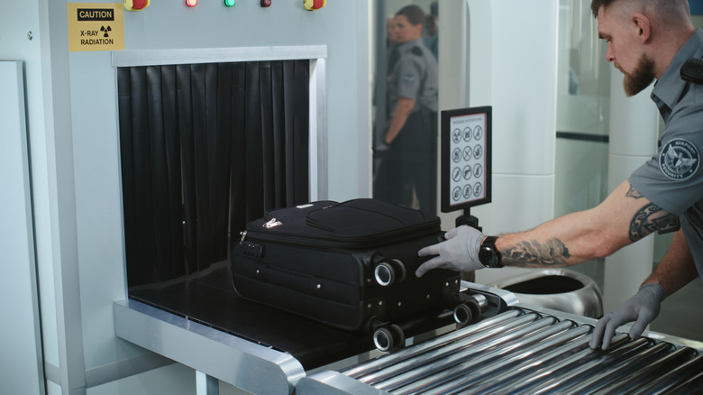 TSA officer placing a laptop bag through a scanner