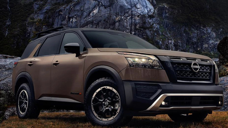 Brown and black 2025 Nissan Pathfinder parked on grass with rocky outcrop behind it