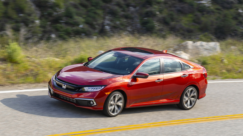 A red Honda Civic in the sedan body style from the 2021 year moving along a two-lane road with a solid yellow division line visible.
