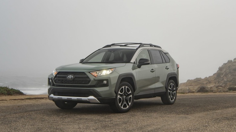 A matte green Toyota RAV4 from the new generation 2021 lineup standing on the shores of a water body on a foggy morning.