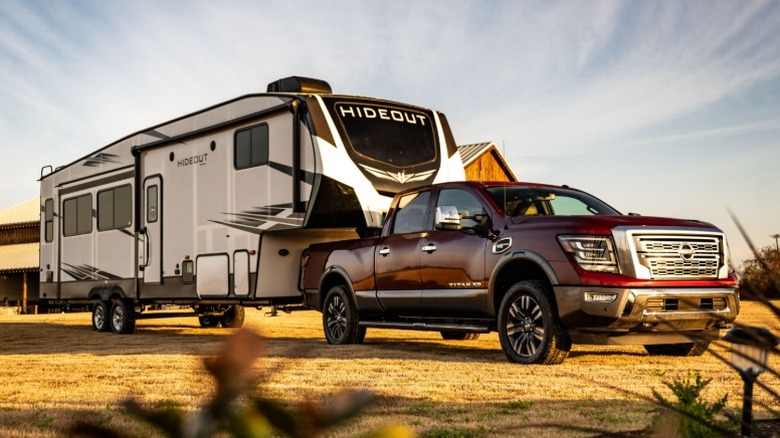Red Nissan Titan XD parked on dirt with a travel trailer attached