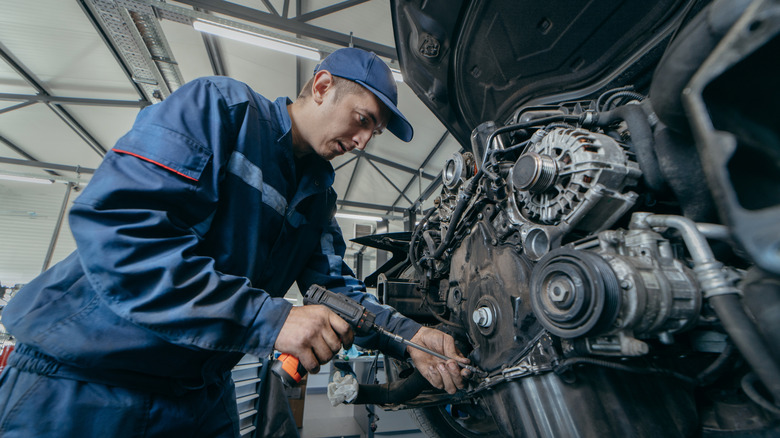 Front view of mechanic repairing front of vehicle engine in service bay.