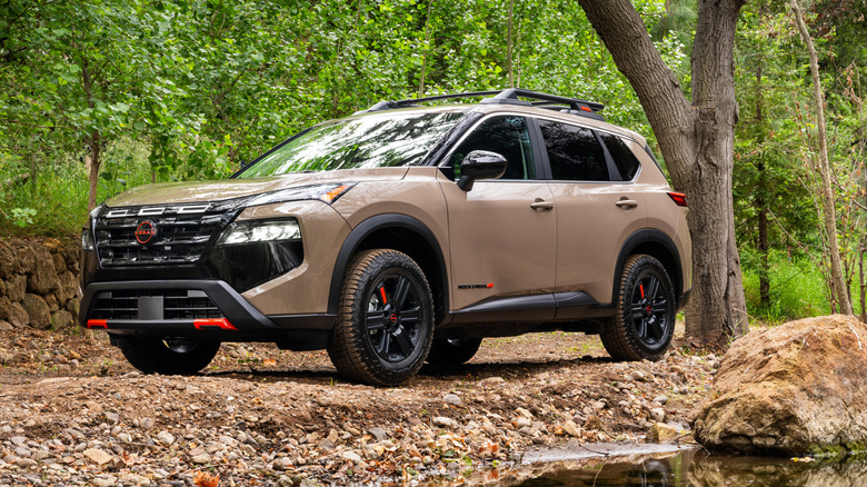 Front 3/4 view of tan-colored 2026 Nissan Rogue SUVs parked near creek.