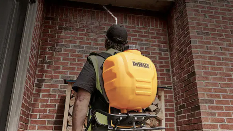 A man with a Dewalt backpack sprayer spraying the exterior of a brick building