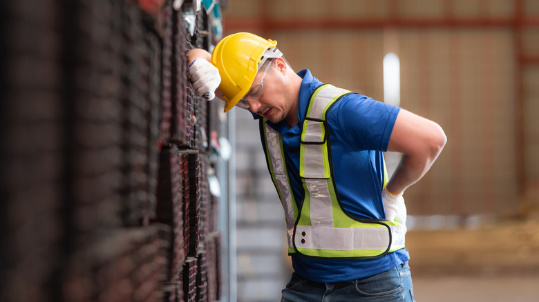 Man holding his back in pain standing in a warehouse