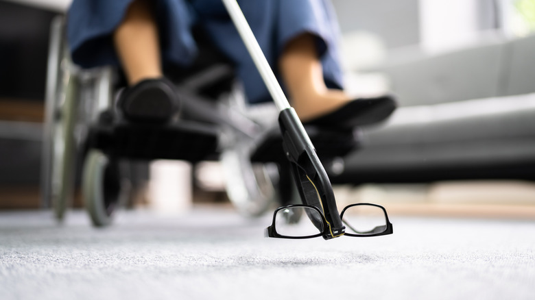 A person in a wheelchair using a grabbing tool to reach a pair of glasses on the floor