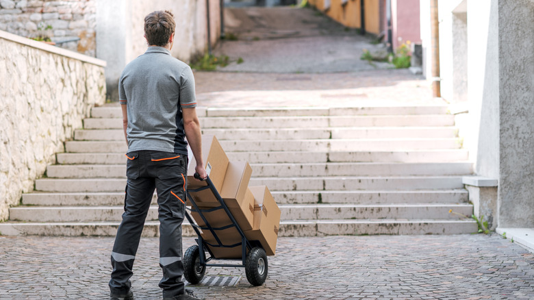 A man with boxes on a hand truck facing several flights of stairs outdoors