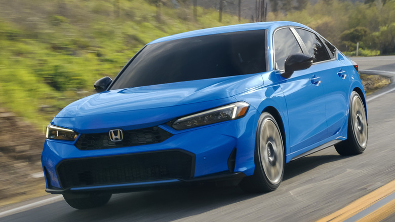 Front 3/4 view of Honda Civic hatchback driving on winding road in forested setting