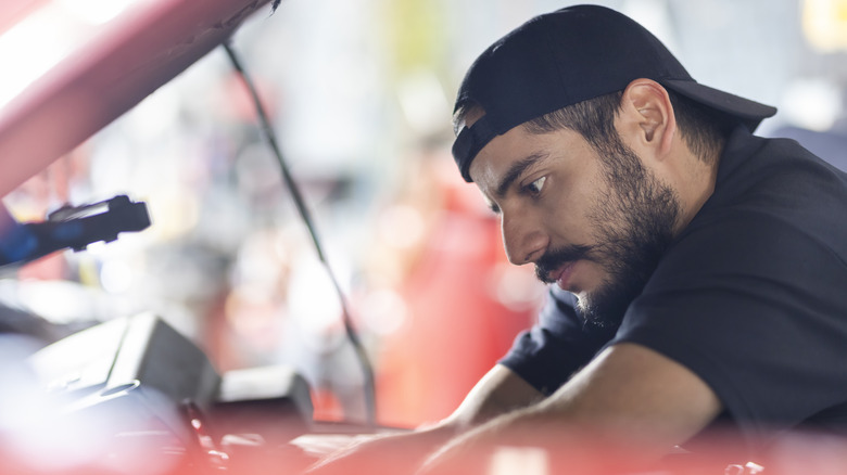 Close shot of man working on car with hood open