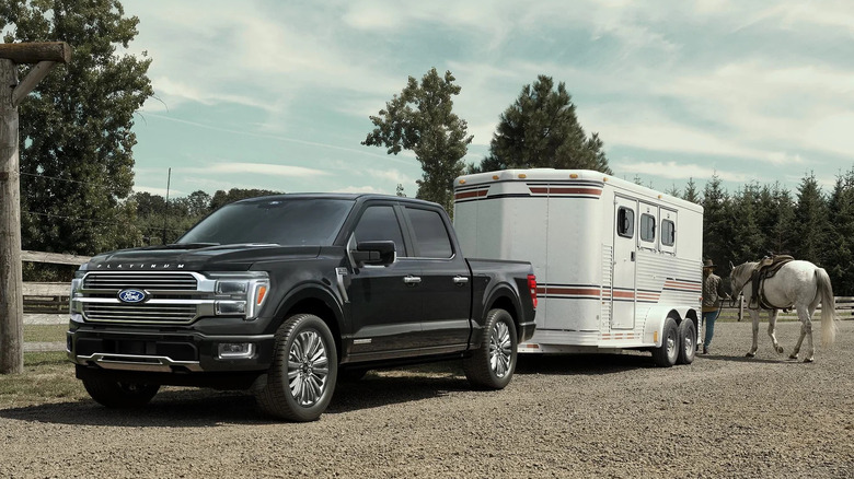 Front 3/4 view of black Ford F-150 Hybrid towing horse trailer at ranch.