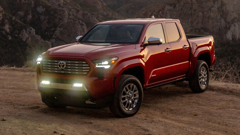 Front 3/4 view of red Toyota Tacoma Limited parked on dirt trail at dusk.