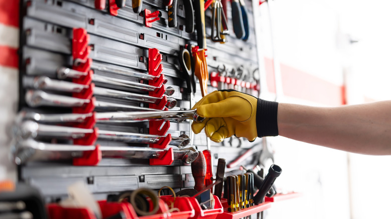 A mechanic wearing yellow gloves carefully removing tools from an organized tool rack.