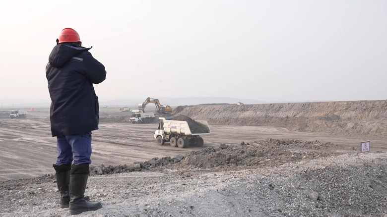 A person standing at an open-pit mine with autonomous trucks and machinery in the distance
