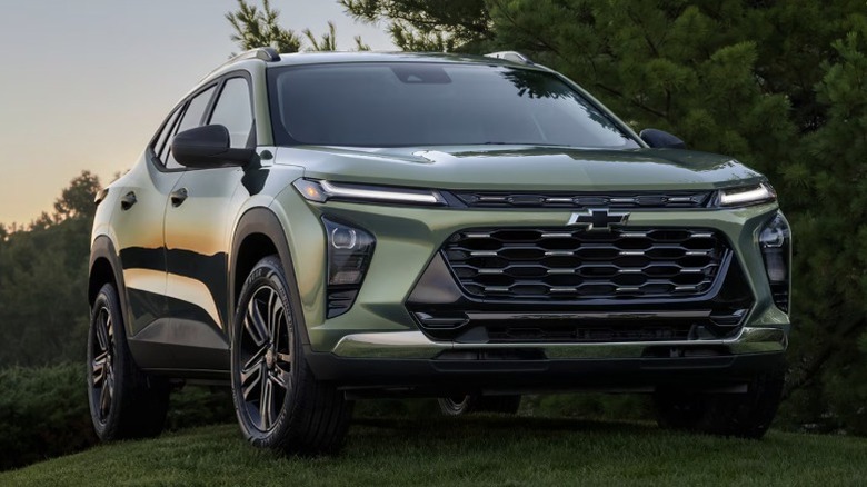 A dark green Chevrolet Trax parked on grass, trees in the background