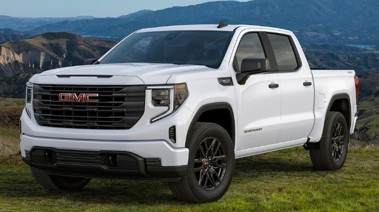 A white 2026 GMC Sierra 1500 parked on grass, with mountains in the background