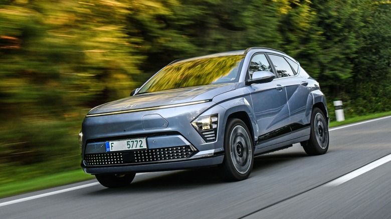 Gray Hyundai Kona Electric driving on a road, trees in the background