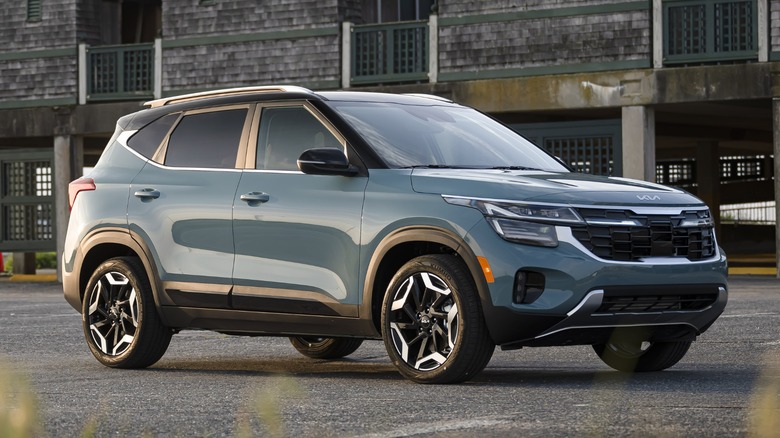 A blue 2024 Kia Seltos parked in front of a gray building