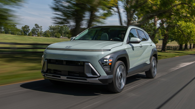 Green Hyundai Kona driving on a leafy rural road