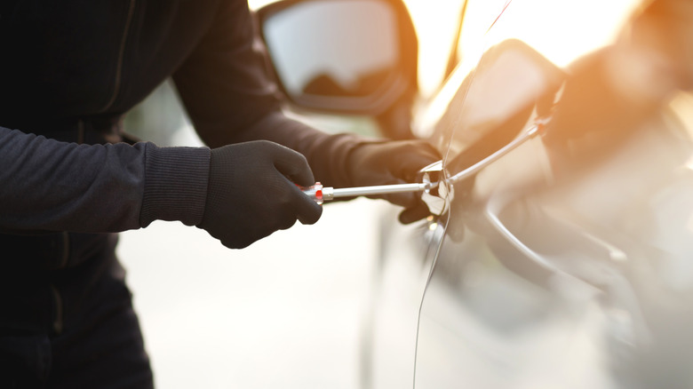 Car thief using screwdriver to break into a car door