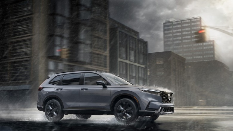 Side shot of a grey 2025 Honda CR-V Sport Touring Hybrid driving through an abandoned city in the rain