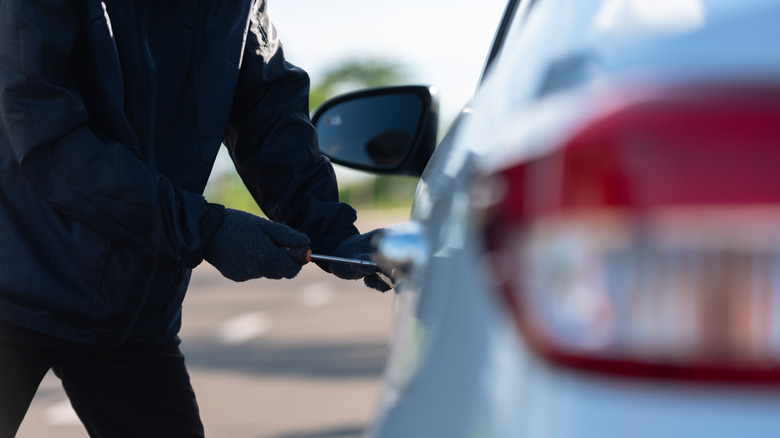A close up shot of a man dressed in all black attempting to pick a car door lock.