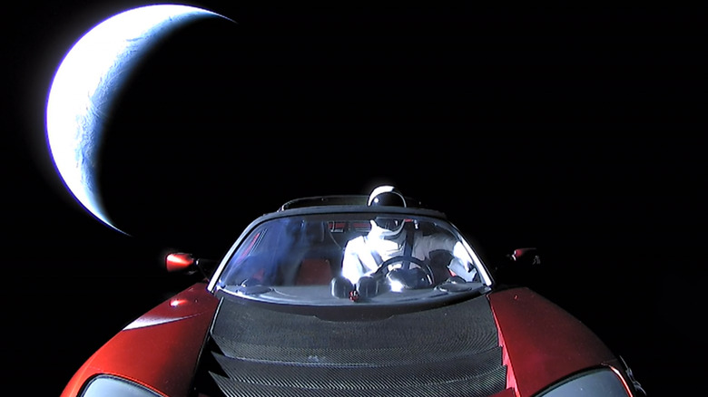 A red Tesla Roadster in space with earth behind it.