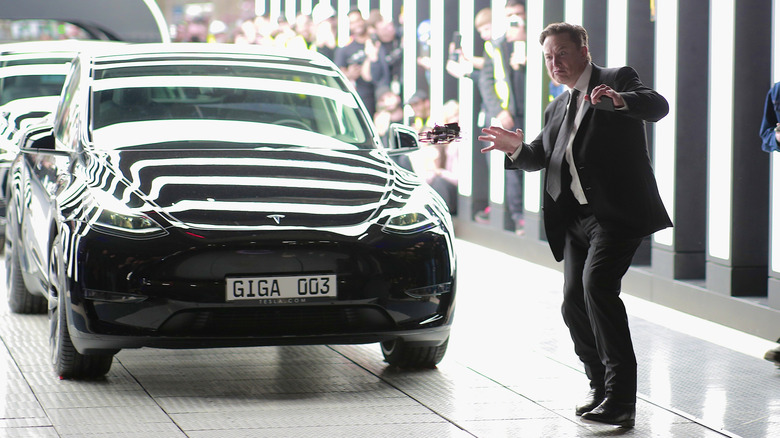 Tesla CEO Elon Musk striking a comical pose in front of a black Tesla Model 3