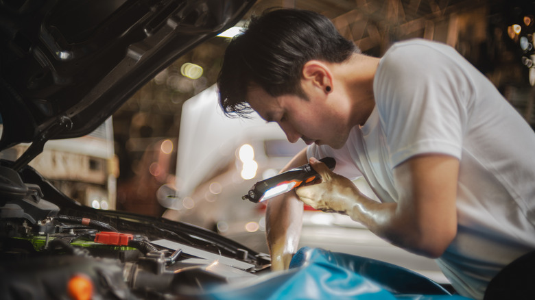 Young mechanic examining car engine with flashlight